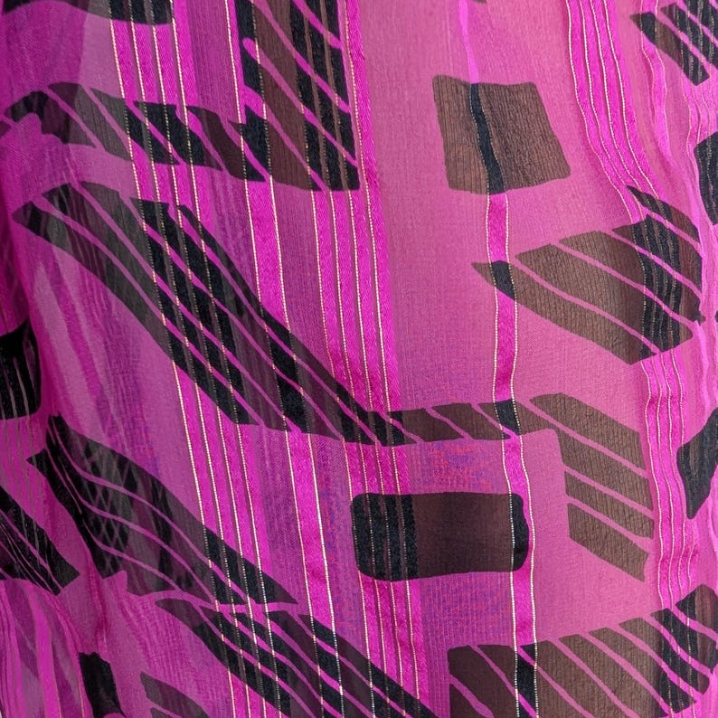 May include: A sheer, magenta fabric with a repeating pattern of black, brown, and gold geometric shapes and vertical stripes. The fabric has a delicate, flowing appearance, with light reflecting off the gold accents.