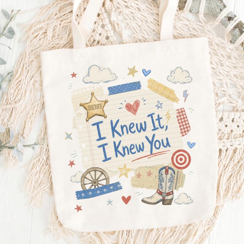 Op de afbeelding: Een cr&egrave;mekleurige canvas tas met een centrale afbeelding op een achtergrond van gelinieerd papier met de tekst "I Knew It, I Knew You". Het ontwerp bevat een gouden sheriffster, een cowboylaars, een wagenwiel, hartjes, sterren en wolken.