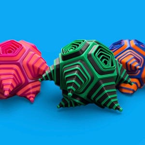 May include: Three abstract, geometric sculptures in shades of pink, green, and blue-orange. Each has a layered, hexagonal design with pointed protrusions, set against a bright blue background.