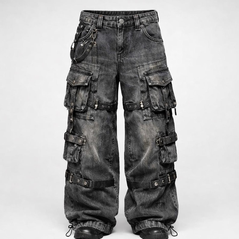 Puede incluir: Pantalones cargo de mezclilla negra descolorida con m&uacute;ltiples bolsillos, correas y hebillas. Los pantalones tienen un dise&ntilde;o de pierna ancha y un detalle de cadena adjunto al trabilla. La mezclilla tiene un aspecto desgastado.