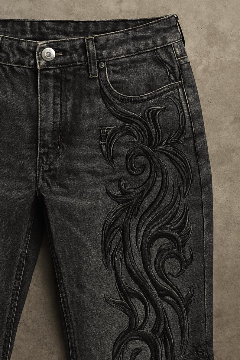May include: Close-up of black denim jeans with an intricate, embossed floral design on the right leg. The jeans have a classic five-pocket design with a button and zipper closure. The dark wash denim has a slightly faded appearance.