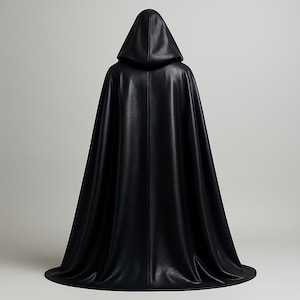 Op de afbeelding: Een zwarte cape met capuchon, waarschijnlijk gemaakt van een glad, leerachtig materiaal. De cape heeft een volledige capuchon en reikt tot de vloer. De afbeelding is van achteren genomen en toont het ontwerp en de textuur van de cape. De cape is effen zwart.