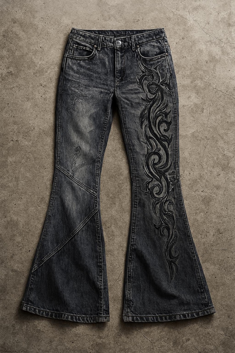 May include: Dark gray denim bell-bottom jeans with a faded wash. The jeans feature a decorative black embroidered design on the side of the leg. The jeans have a classic five-pocket design.