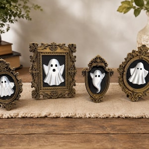 May include: Four ornate, antique-style gold frames of varying shapes and sizes, each containing a black background with a white, three-dimensional ghost figure featuring two black eyes and a small black mouth, displayed as a set of wall decor.