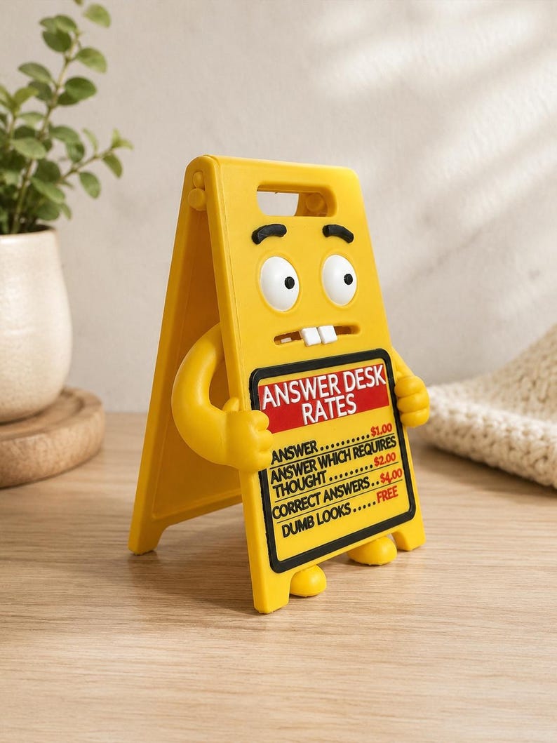 May include: A yellow A-frame sign character with a cartoon face, two white teeth, and arms holding a black sign board. The text reads: ANSWER DESK RATES, ANSWER $1.00, ANSWER WHICH REQUIRES THOUGHT $2.00, CORRECT ANSWERS $4.00, DUMB LOOKS FREE.
