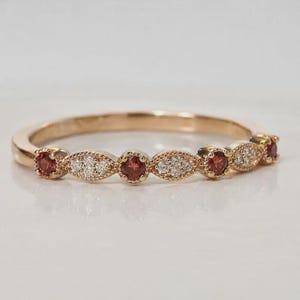 Könnte beinhalten: Ein Ring aus Roségold mit einem abwechselnden Muster aus runden roten Granatsteinen und marquiseförmigen Clustern aus kleinen weißen Diamanten. Das Metallband hat eine polierte Oberfläche und die Steine sind in einer symmetrischen Anordnung.