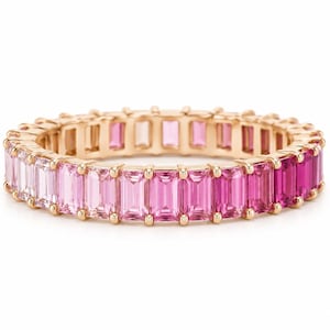 May include: A gold eternity band featuring a continuous row of baguette-cut gemstones in a gradient of pink hues, transitioning from pale blush to deep magenta. The stones are set in a polished gold metal frame with small prongs securing each gem.