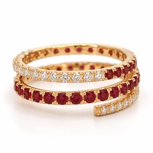 May include: A gold bypass ring featuring a multi-row spiral design. The band is set with alternating sections of round, brilliant-cut clear white stones and deep red circular stones, creating a continuous, layered appearance around the finger.