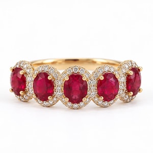 May include: A gold ring featuring five oval-cut red rubies arranged in a row. Each ruby is surrounded by a halo of small, round, clear white diamonds set in gold. The band is made of polished yellow gold, creating a continuous, elegant design.