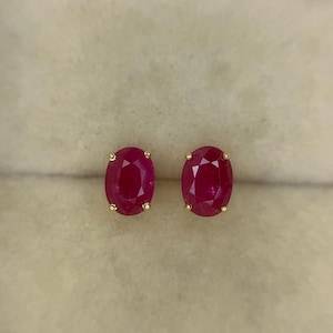 以下が含まれることがあります： オーバルカットのルビーのスタッドピアス。ルビーは深い赤色で、金でセットされています。ピアスはニュートラルな背景に表示されています。