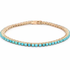 Könnte beinhalten: Ein goldfarbenes Armband mit einer Reihe kleiner, runder, türkisfarbener Edelsteine. Das Armband hat ein filigranes, verbundenes Design und einen sicheren Verschluss. Schmuck.