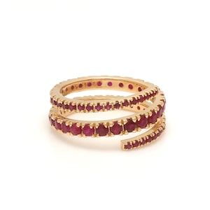 May include: A gold-toned ring with a spiral design, adorned with numerous small, vibrant red gemstones. The ring's design features two intertwined bands, creating a unique and eye-catching piece of jewelry.