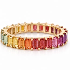 Könnte beinhalten: Ein Goldring als Eternity-Band mit einer durchgehenden Reihe von im Baguette-Schliff geschliffenen Edelsteinen in einem lebendigen Regenbogenverlauf, der von Hellgrün und Gelb über Orange und Rot bis hin zu Pink und Dunkelviolett reicht.