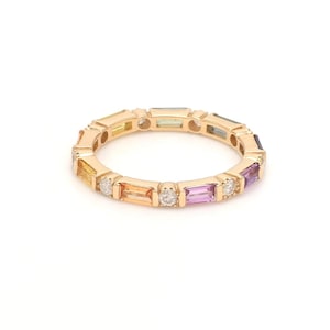 May include: A gold ring with a continuous band of colourful rectangular gemstones, including yellow, orange, pink, and blue, and small, round, clear stones. The ring's design features gemstones set around the entire circumference.