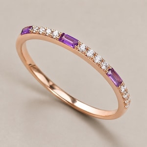 Op de afbeelding: Een roségouden ring met een dunne, gepolijste metalen band, bezet op de bovenste helft met afwisselend heldere ronde stenen en rechthoekige paarse amethiststenen, wat zorgt voor een verfijnde en gebalanceerde uitstraling.