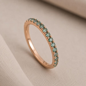 Könnte beinhalten: Ein Ring aus Roségold mit einer Reihe kleiner, runder, blaugrüner Edelsteine, die in einer Krappenfassung entlang der oberen Hälfte des Rings angeordnet sind. Das Metall hat ein warmes, metallisches Finish und die Steine bilden eine Linie.