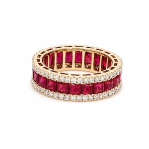 May include: A gold ring with two rows of square-cut, vibrant red gemstones and a row of small, sparkling white gemstones in between. The ring is set against a white background, highlighting its intricate design and luxurious appearance.
