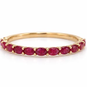 Puede incluir: Un anillo de banda de oro que presenta una fila continua de pequeños rubíes de color rojo intenso, tallados en forma ovalada y engastados en garras individuales. El metal tiene un acabado pulido y las piedras están dispuestas simétricamente.