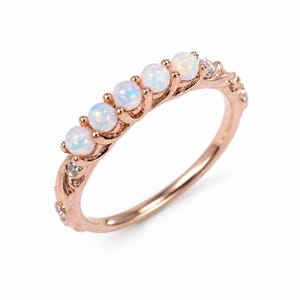May include: Rose gold ring featuring five round opal gemstones. The ring has a delicate design with small accent stones on the band. The opals have a milky white color with flashes of blue and green.