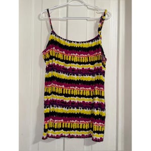 May include: A sleeveless tank top featuring a horizontal pattern of alternating stripes in bright yellow, magenta, and black. The garment has thin spaghetti straps and a straight neckline, hanging on a white plastic hanger against a white door.