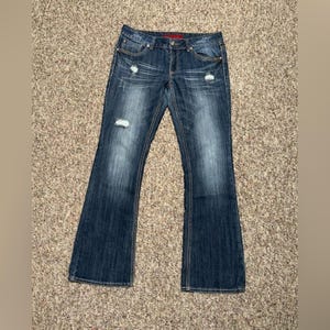 May include: Dark blue denim jeans featuring a bootcut silhouette, a mid-rise waist, and a classic five-pocket design. The fabric displays a faded wash effect on the thighs and knees, with intentional distressed areas and frayed detailing.