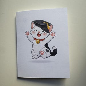 May include: A greeting card featuring a cartoon cat wearing a graduation cap and a red collar with a gold bell. The cat is black and white, with its paws raised in a celebratory pose. The background is plain white.