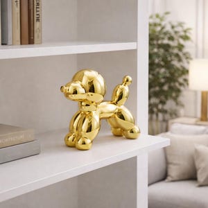 Peut inclure: Une sculpture dorée en forme de caniche, inspirée des ballons. La figurine de chien décorative est posée sur une étagère blanche, mettant en valeur sa surface métallique réfléchissante. Le design rappelle un animal en ballon.
