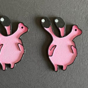 May include: Four pink fabric patches in a cartoonish creature design. Each patch features a pink body, black head with two white-dotted eyes, and a black outline. The patches are arranged horizontally on a gray surface.
