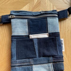 May include: A denim patchwork fanny pack with a zippered top and front pocket. The bag features various shades of blue denim, with a small white tag that reads "Grendipity". The strap is black.