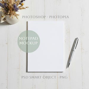 Peut inclure: Maquette de bloc-notes blanc avec un stylo argenté sur une surface en bois blanc. Le bloc-notes est vierge, prêt pour la conception. Un petit vase avec des fleurs séchées est dans le coin supérieur gauche. Le texte sur l'image dit "Photoshop - Photopea", "Notepad Mockup", et "PSD Smart Object - PNG".
