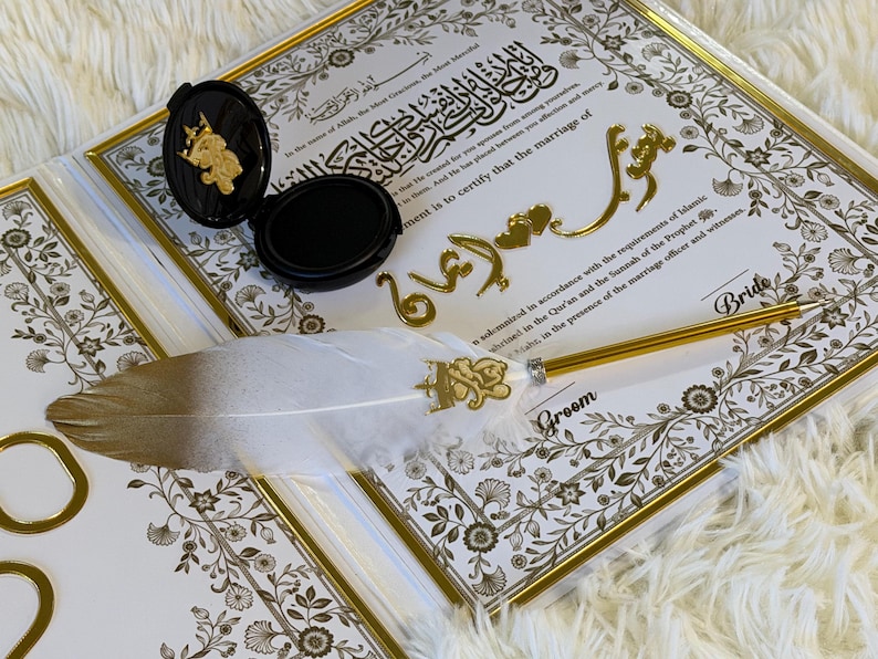 May include: A wedding certificate with gold accents, a decorative feather pen, and a black ink pad. The certificate has ornate floral borders and gold lettering. The pen has a white feather and gold details.