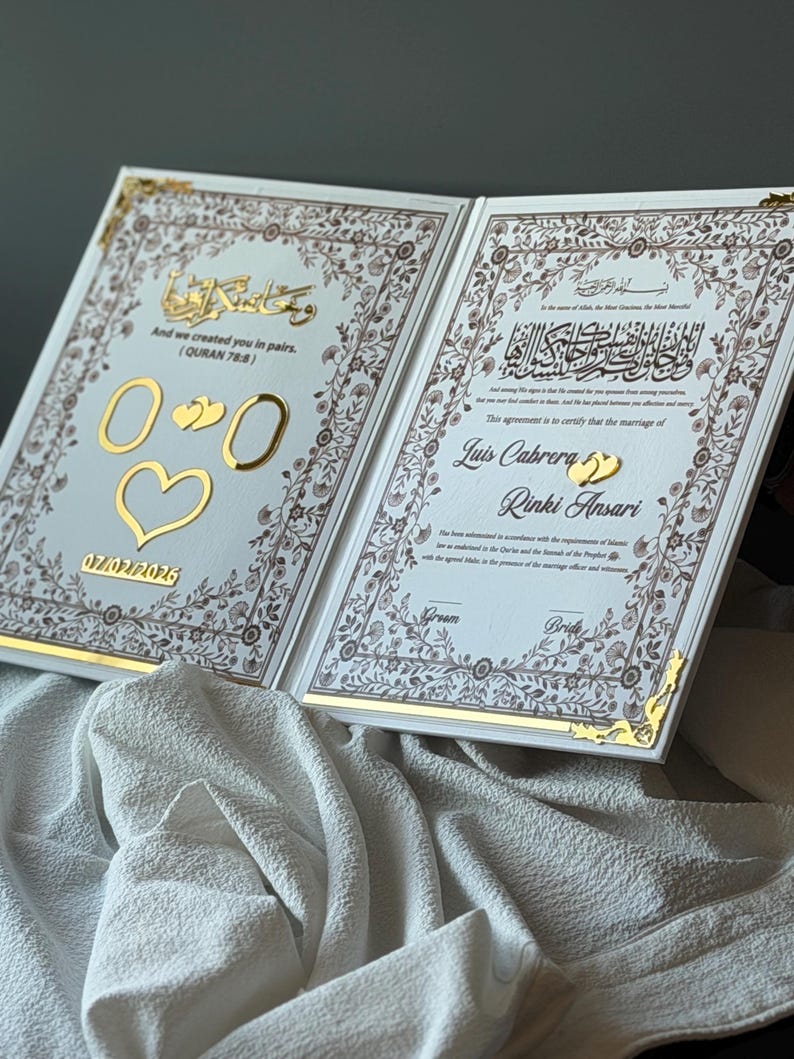 May include: An open, white wedding certificate with gold accents and floral borders. The left page has gold numbers, hearts, and the date 07/02/2026. The right page has Arabic script and the names Luis Cabrera and Rinki Ansari.