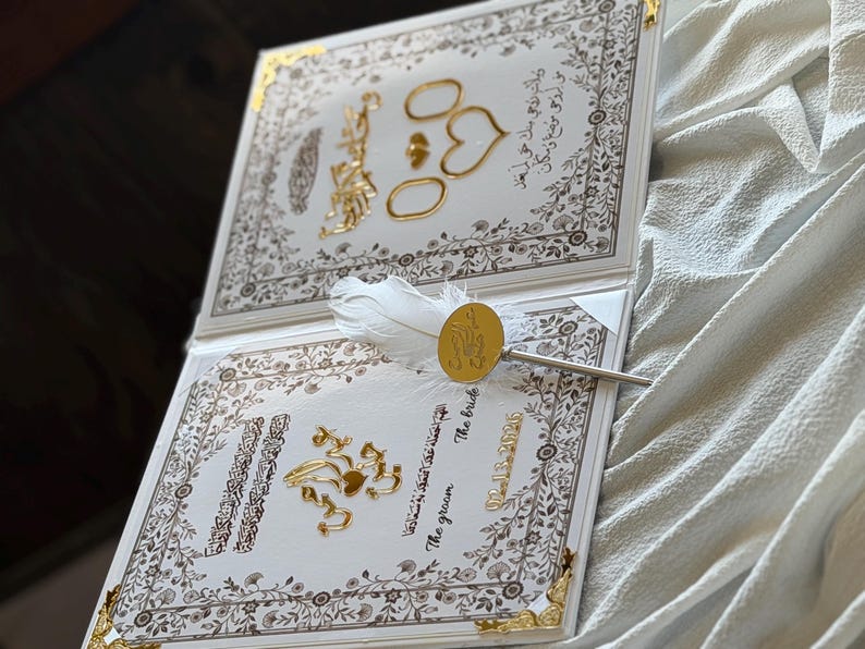 May include: A wedding invitation with gold accents and ornate floral borders. The invitation features gold rings, hearts, and decorative elements. A pen with a white feather and gold seal rests on the invitation. The date 02-15-2020 is visible.