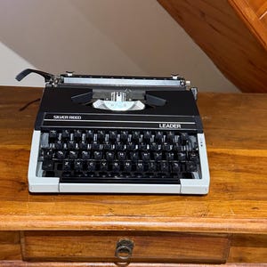 Máquina de escribir vintage plateada con guía de lengüeta, bicolor (rojo/negro), totalmente funcional.