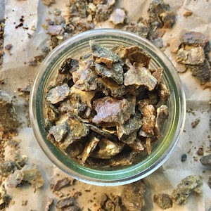 May include: A clear glass jar filled with irregularly shaped, dark brown and tan pieces. The jar sits on a light brown, textured surface, with similar pieces scattered around it. The image is taken from a top-down perspective.