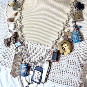 Könnte beinhalten: Eine silberfarbene Charm-Halskette mit einer Vielzahl eklektischer Anhänger, darunter ein kleines Porträt, ein Miniatur-Taschenmesser, eine blau bemalte Figur, ein Metallschild mit dem Text SIMPLIFY und ein rechteckiges Stück mit Berglandschaft.