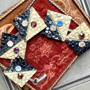 Könnte beinhalten: Ein Vintage-Armband aus schwarzem und weißem Kunststoff mit geometrischem Design. Das Armband ist mit Strasssteinen verziert und hat einen silbernen Verschluss.