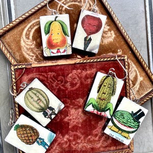 May include: Five pairs of earrings featuring different fruits and vegetables. Each earring is a small rectangular piece of wood with a painted image of a pear, beetroot, corn, watermelon, and pineapple. The earrings are all in a vintage style and have a whimsical feel.