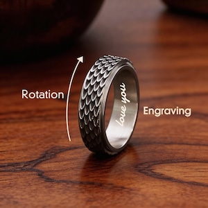 Op de afbeelding: Een zilverkleurige ring met een textuur, schubachtig patroon op de buitenste band. De binnenband heeft de gegraveerde woorden "love you". De afbeelding toont ook de woorden "Rotatie" en "Graveren".