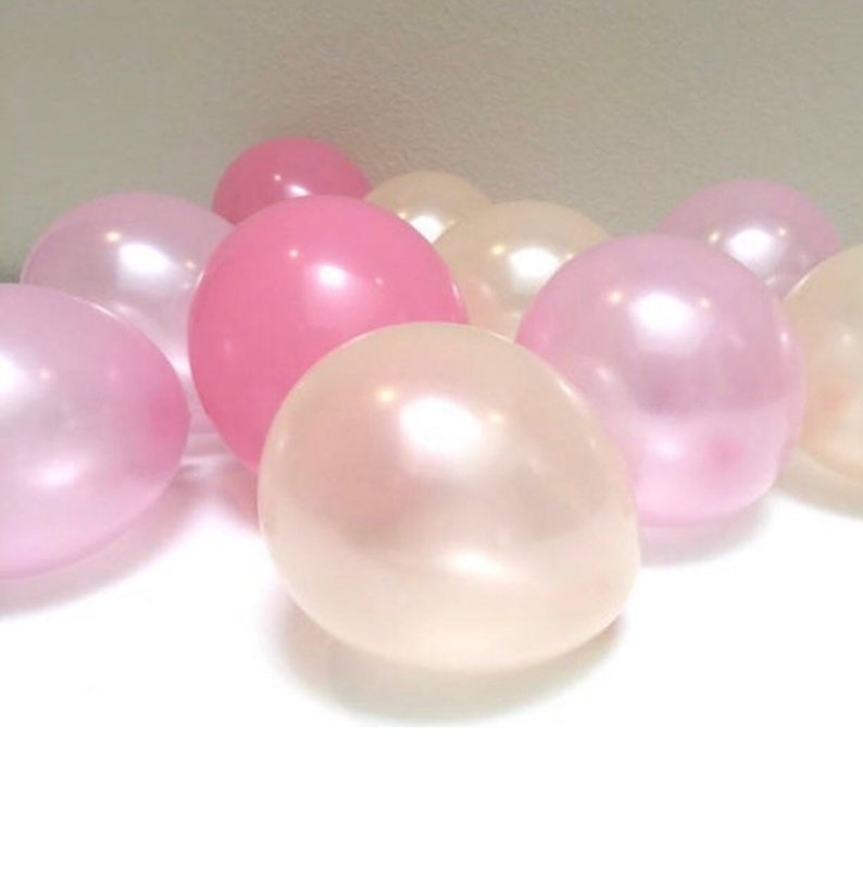 May include: A collection of pink and pearl-colored balloons. The balloons vary in shades from light pink to a deeper rose color, with a pearlescent sheen. The balloons are clustered together, creating a soft, celebratory aesthetic.