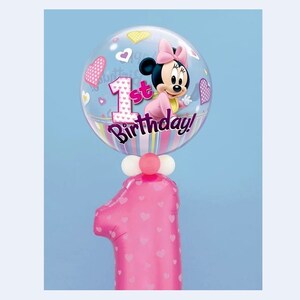 May include: A pink number one balloon with heart patterns, topped with a clear balloon featuring Minnie Mouse and the text "1st Birthday!". The clear balloon has heart and star accents, with a pink bow on Minnie's head.
