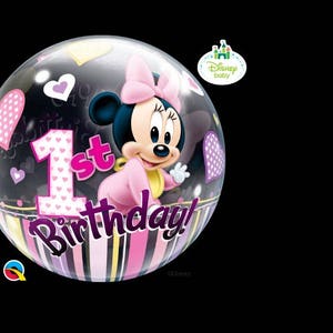 May include: A clear bubble balloon featuring Minnie Mouse in a pink outfit, with the text "1st Birthday!" in pink and purple. The balloon has heart and star decorations, and a striped bottom. A Disney Baby logo is visible.
