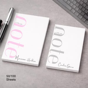 Könnte beinhalten: Zwei weiße Notizblöcke mit dem Wort "Note" in Rosa und Grau. Der rosa Notizblock hat den Namen "Marianna Hudson" darunter aufgedruckt. Der graue Notizblock hat den Namen "Caroline Garcia" darunter aufgedruckt. Beide Notizblöcke haben den Satz "a little note" über dem Wort "Note".