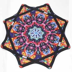 May include: A set of two star-shaped trivets with a vibrant, colorful mandala design. The trivets feature a black border and a complex pattern of red, blue, yellow, and purple hues. The trivets are likely made of fabric and are designed to protect surfaces from heat.