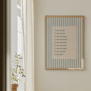 May include: A framed print with a light wood frame. The background has vertical blue and white stripes. A textured, off-white paper with the words "I am kind, I am brave, I am strong, I am capable, I am worthy, I am chosen, I am enough, I am loved, I am His" is centered.