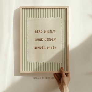 May include: A framed wall art print featuring a light green and white vertical striped background. Centered is a textured cream-coloured paper cutout with the brown text: READ WIDELY, THINK DEEPLY, WONDER OFTEN. The text OAKS & ELLIOT STUDIO appears below.