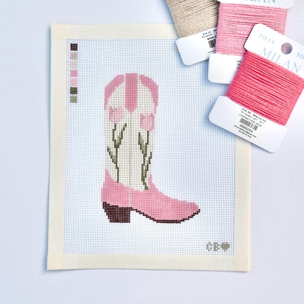 Può includere: Una tela per punto croce con un disegno di stivale da cowboy rosa con accenti floreali verdi. Tre rocchetti di filo beige, rosa chiaro e corallo sono posizionati sopra la tela. La tela ha un bordo color crema e un campionario di colori.