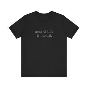 May include: Black t-shirt featuring the text "none of this is normal" in a plain font. The text is centrally placed. The shirt has a crew neck and short sleeves, suitable for casual wear.