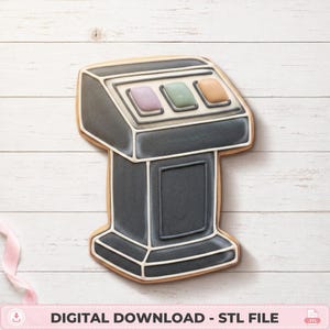 May include: A cookie shaped like a dark gray podium with a slanted top panel featuring three rectangular buttons in light purple, light green, and light orange. The cookie has white icing outlines defining the structure of the podium.