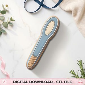 May include: A blue and cream-coloured spoon-shaped object with a textured waffle-patterned base. The item features a smooth, elongated handle and a rounded bowl section, presented as a digital download file for 3D printing, labelled as an STL file.